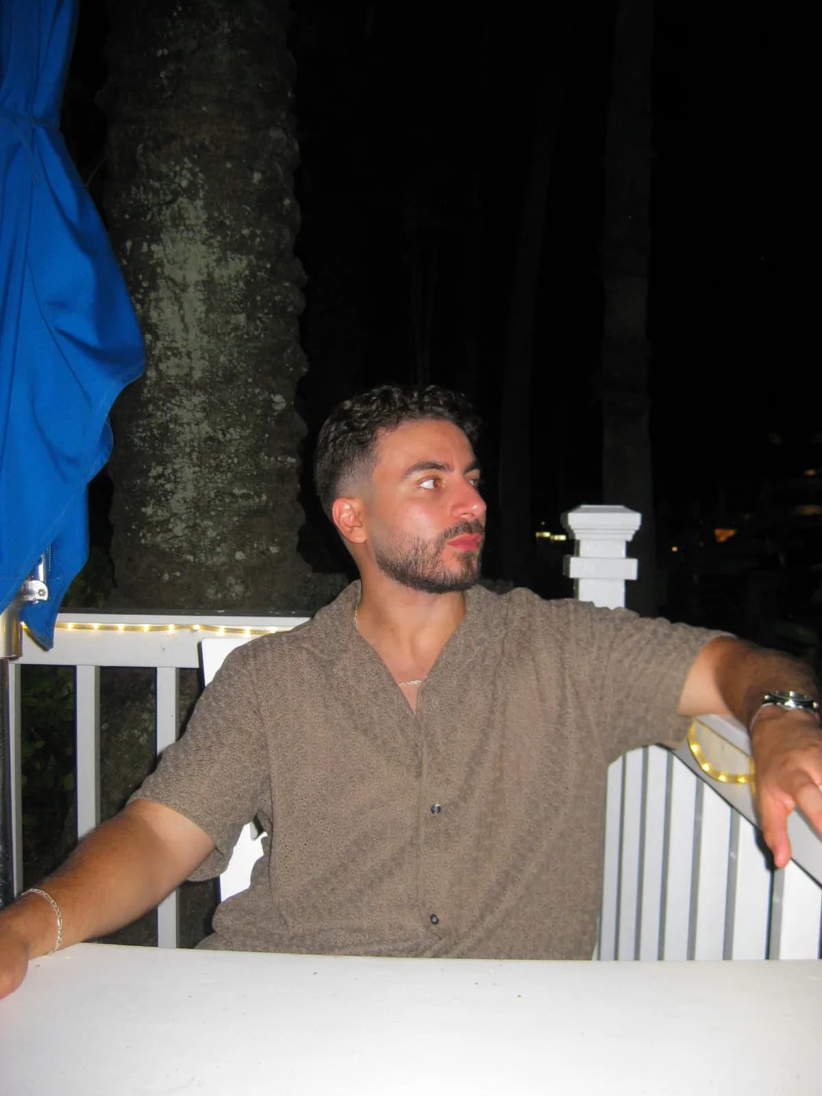 Abdul on a lit deck at night, one arm along the railing, looking off to the side
