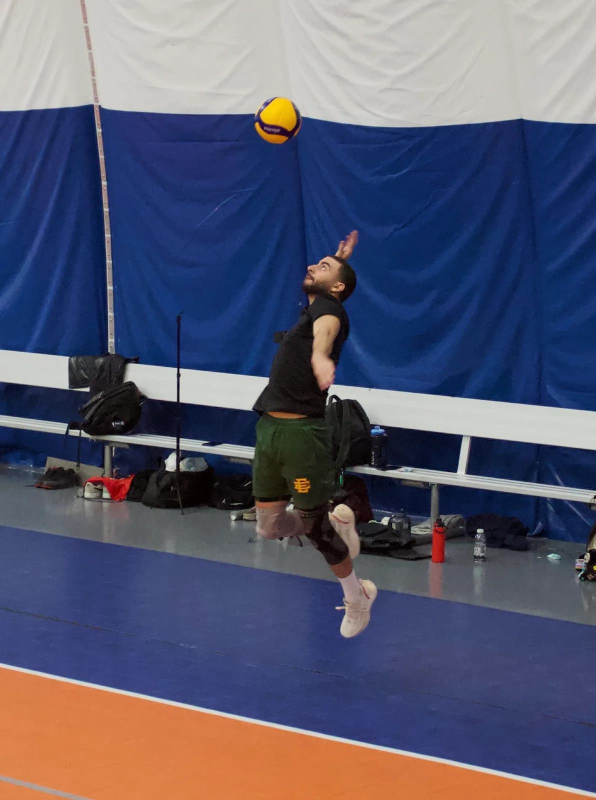 Mid-air at the top of a volleyball serve, ball above an indoor court