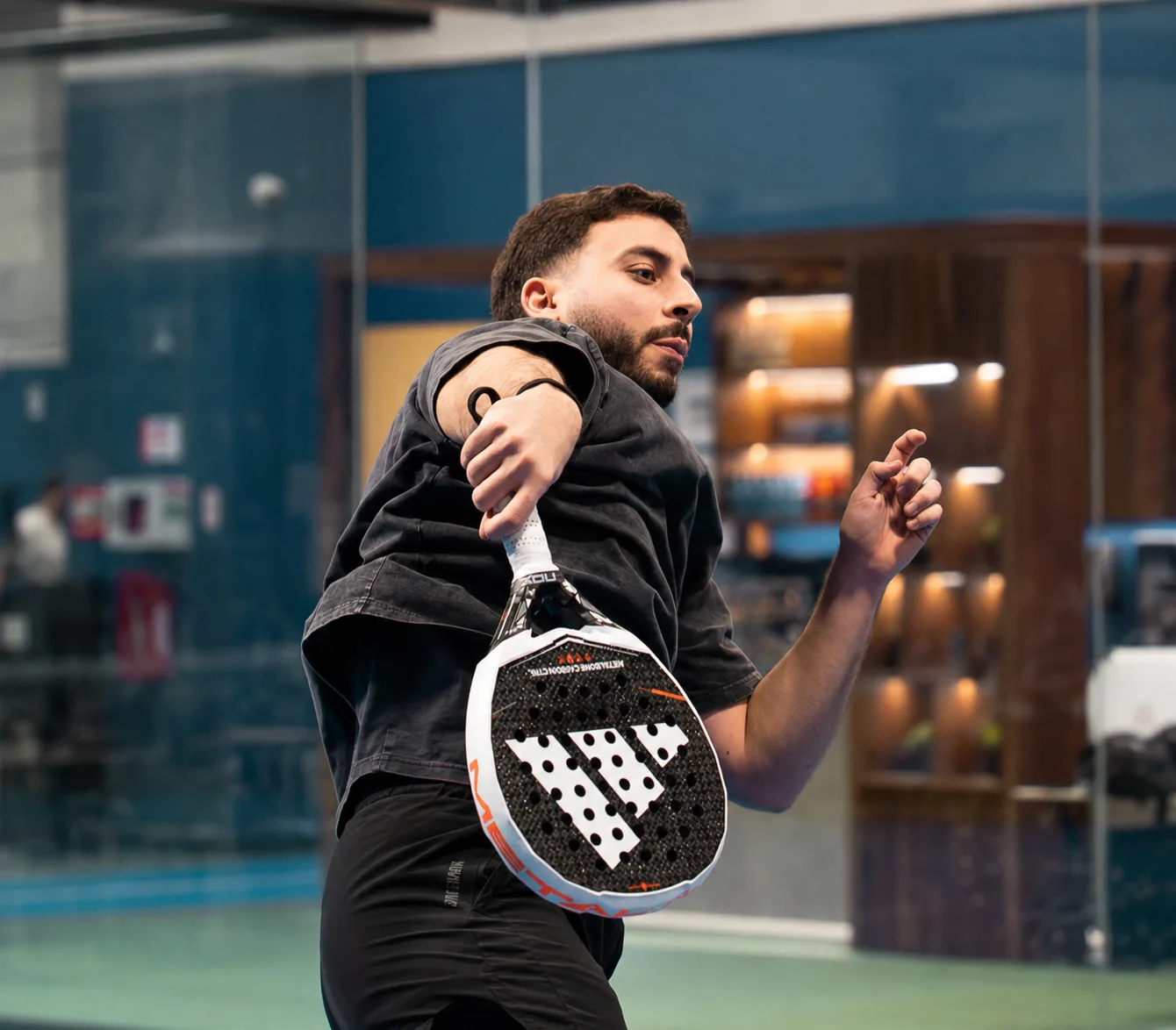 Following through on a padel shot on an indoor court, looking back over the shoulder