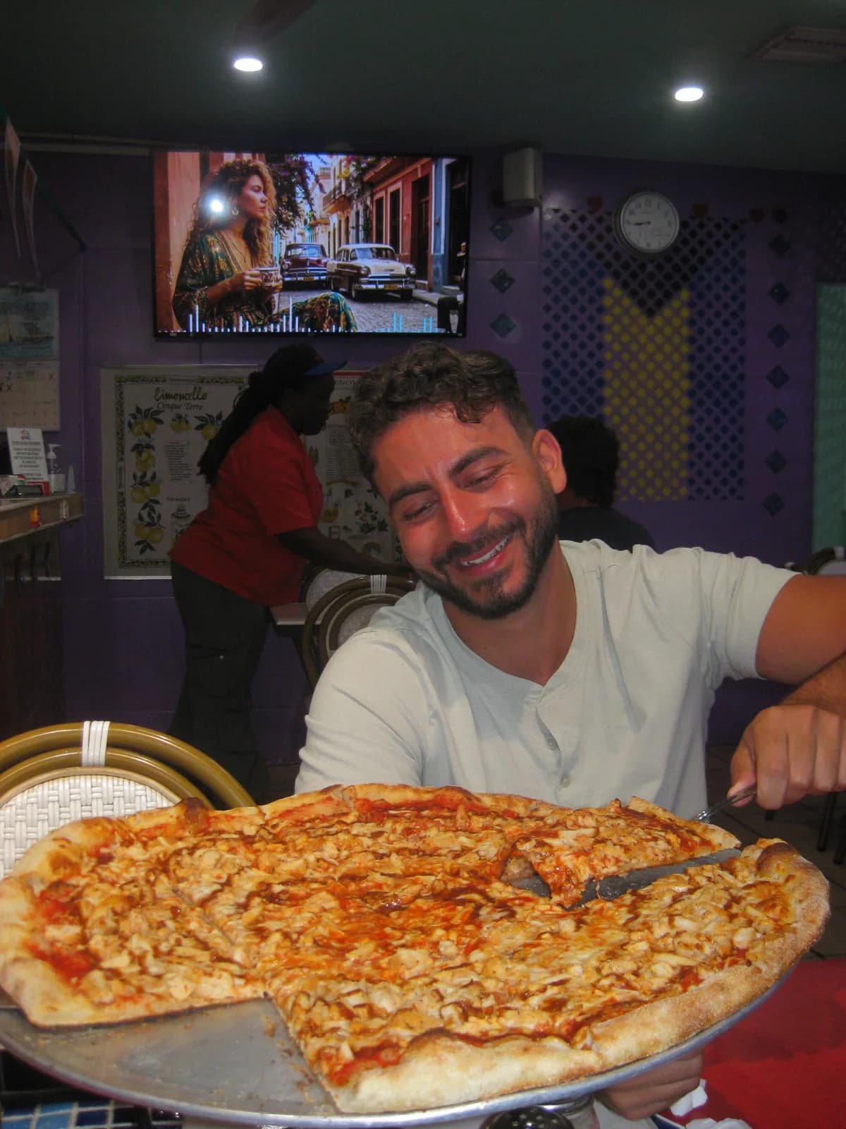 Grinning behind an enormous pizza that fills the whole table